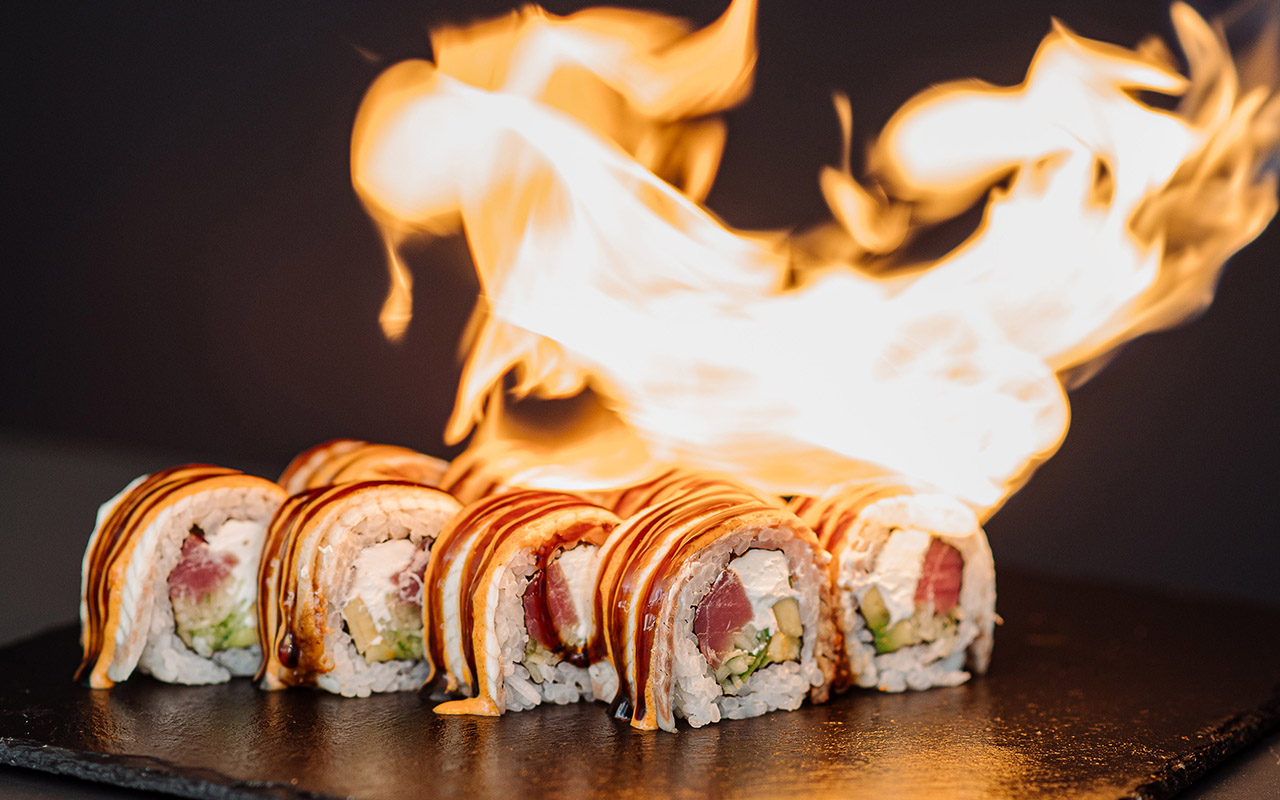 Preparing of sushi rolls with a fire on black background